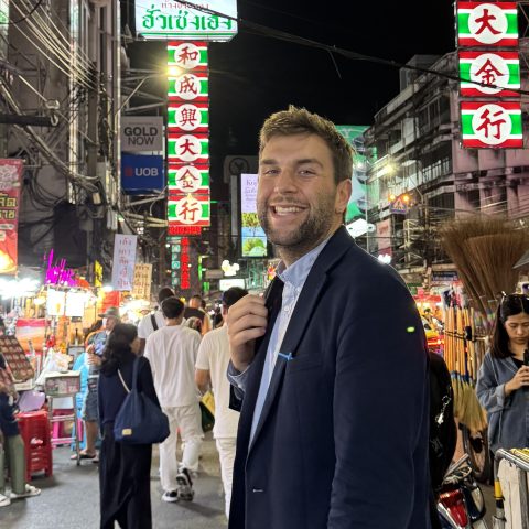 Smiling man in a dark suit poses in a crowded neon-lit night market street unaffected by the bustle behind him? No, that's awkward. Let's craft clean ones.