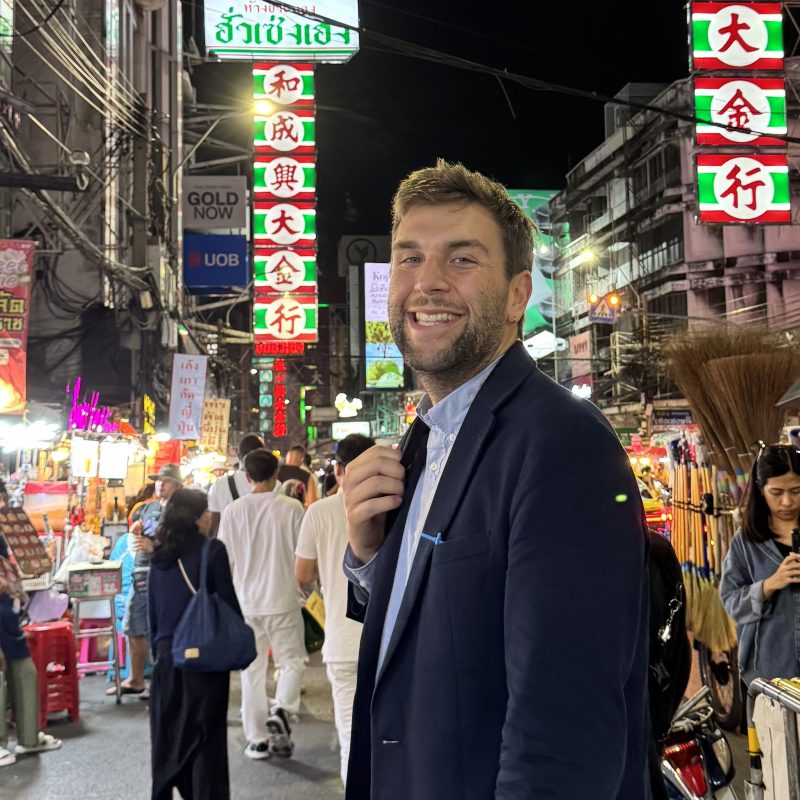 Smiling man in a dark suit poses in a crowded neon-lit night market street unaffected by the bustle behind him? No, that's awkward. Let's craft clean ones.