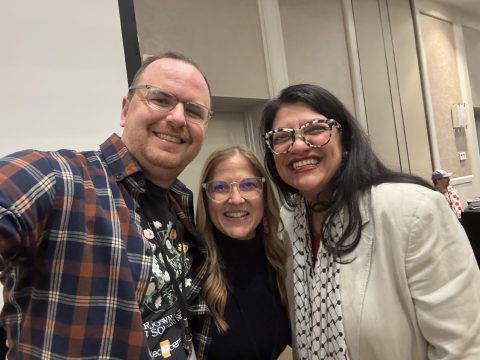 Tres personas haciéndose un selfi en grupo en primer plano en un interior, sonriendo a la cámara (un hombre a la izquierda con camisa a cuadros, dos mujeres en el centro y a la derecha).